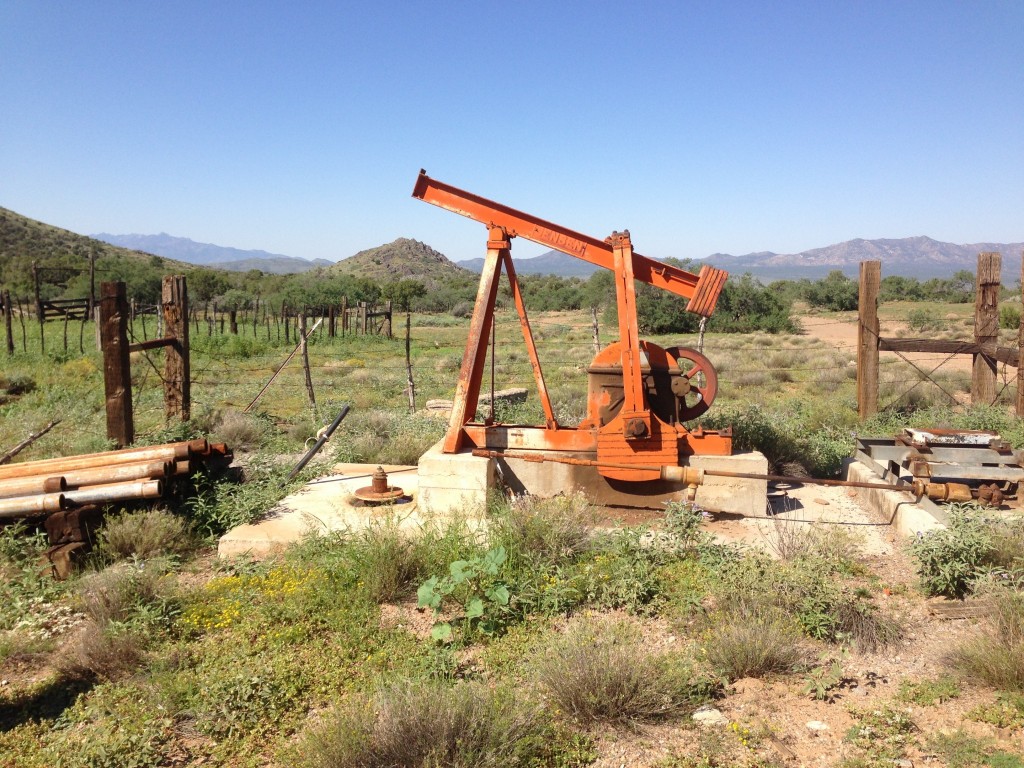 An oil pump jack in a fenced field with mountains in the background